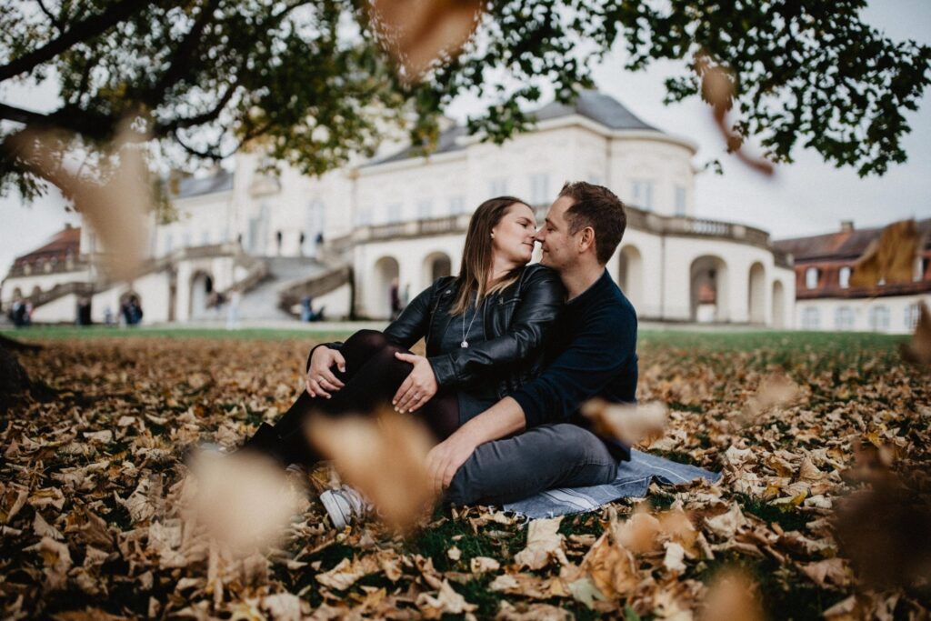 Paar sitzt im Herbstlaub vor Schloss Solitude in Stuttgart